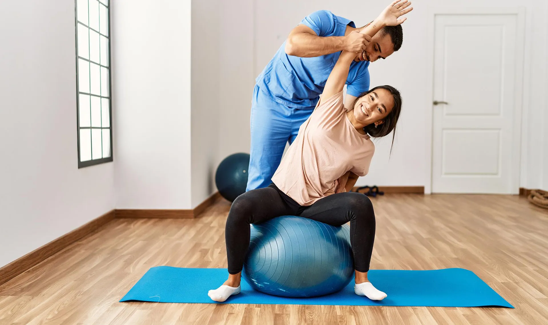 Bewegungstherapie im Reha-Zentrum Hochegg – Physiotherapeut unterstützt Patientin bei Dehnübung auf Gymnastikball